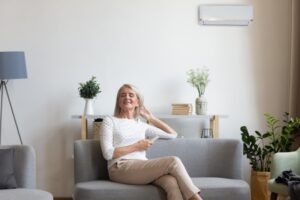 middle-aged-woman-sitting-on-sofa-relaxed-with-mini-split-behind-her