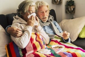 senior-couple-on-couch-woman-blows-nose-while-man-comforts-her